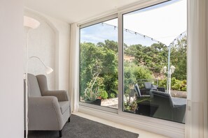 A room with a large sliding glass door leading to a garden, a sofa, and a lamp.