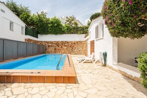 A swimming pool with a stone wall and a stone floor, surrounded by white buildings and greenery.