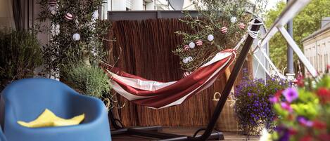 A hammock set up on a wooden deck with a blue chair and a wicker basket nearby.