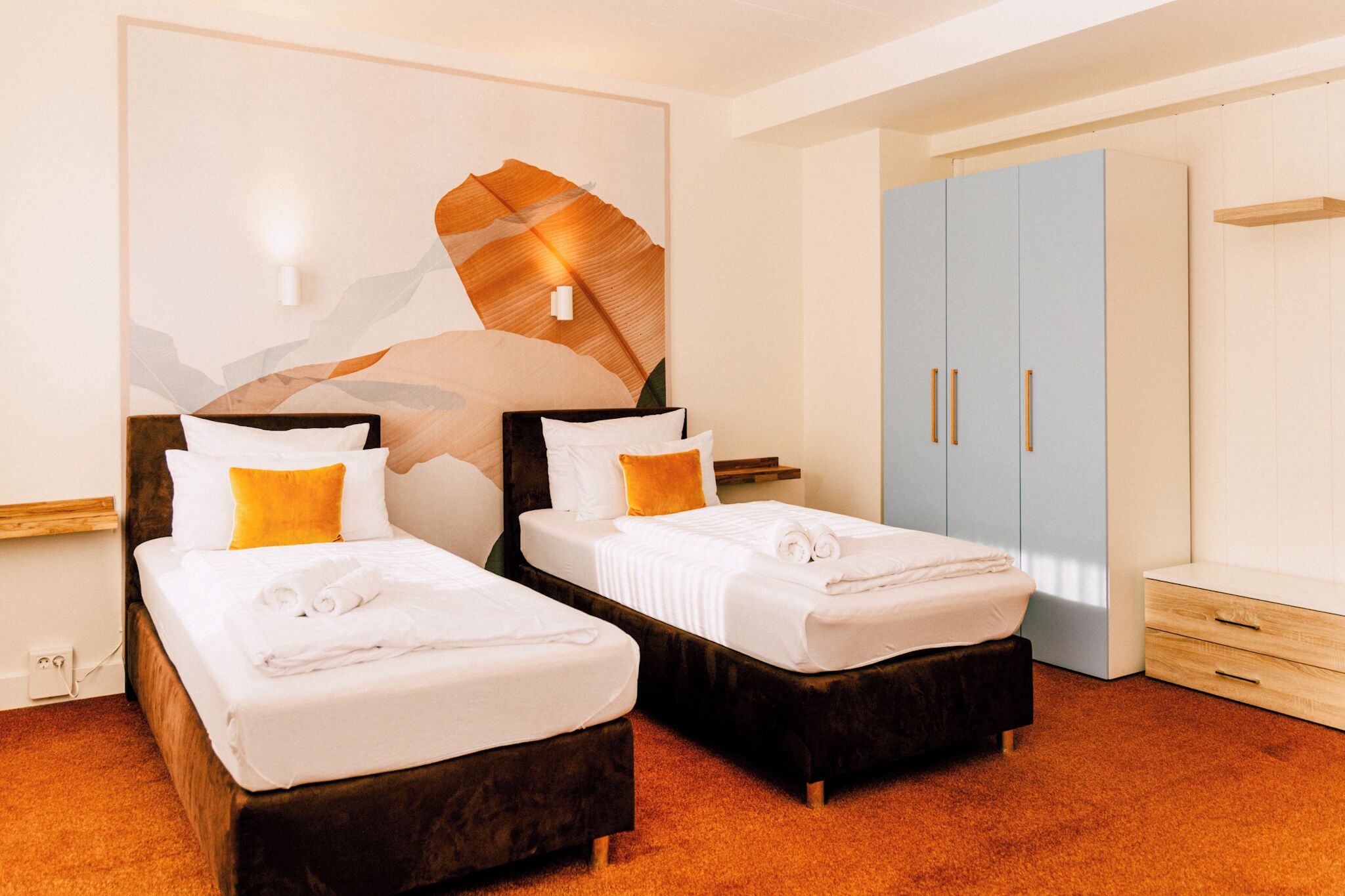 A hotel room with two beds, a large wardrobe, and a wall-mounted light fixture.