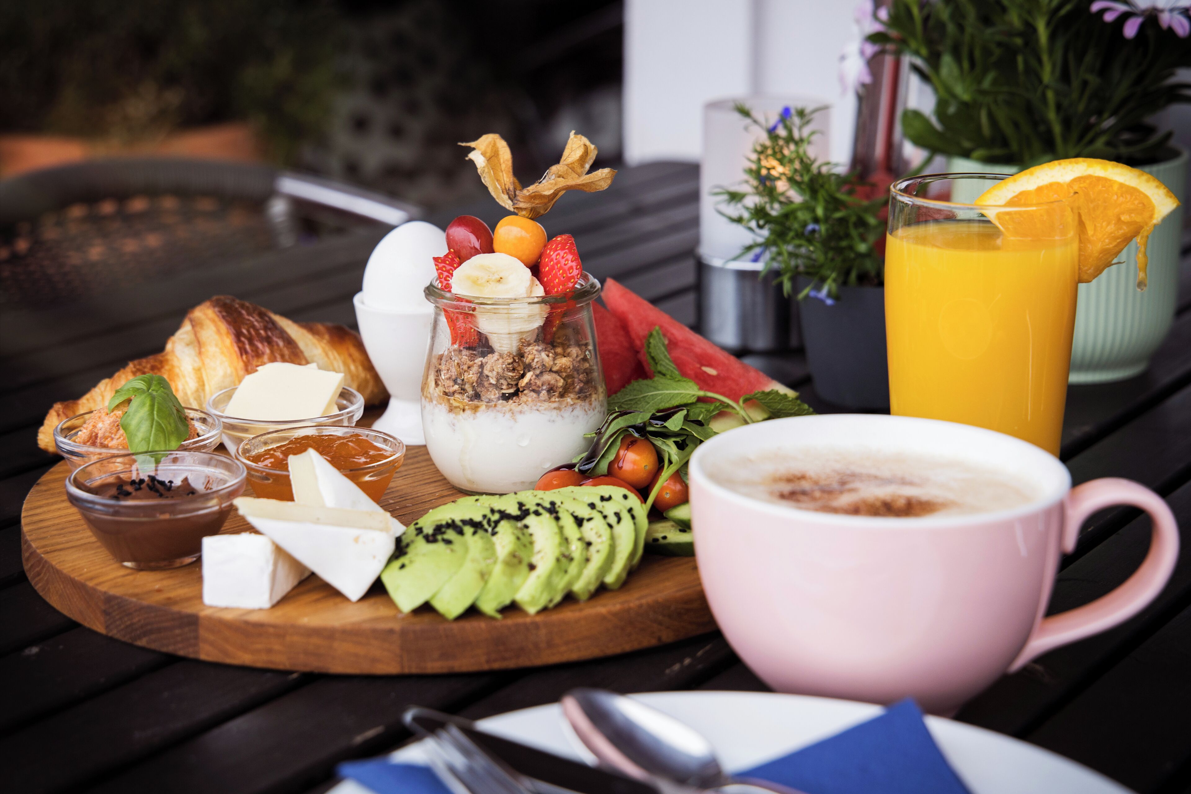 A breakfast setting with croissants, yogurt, fruits, and a glass of orange juice on a wooden table.