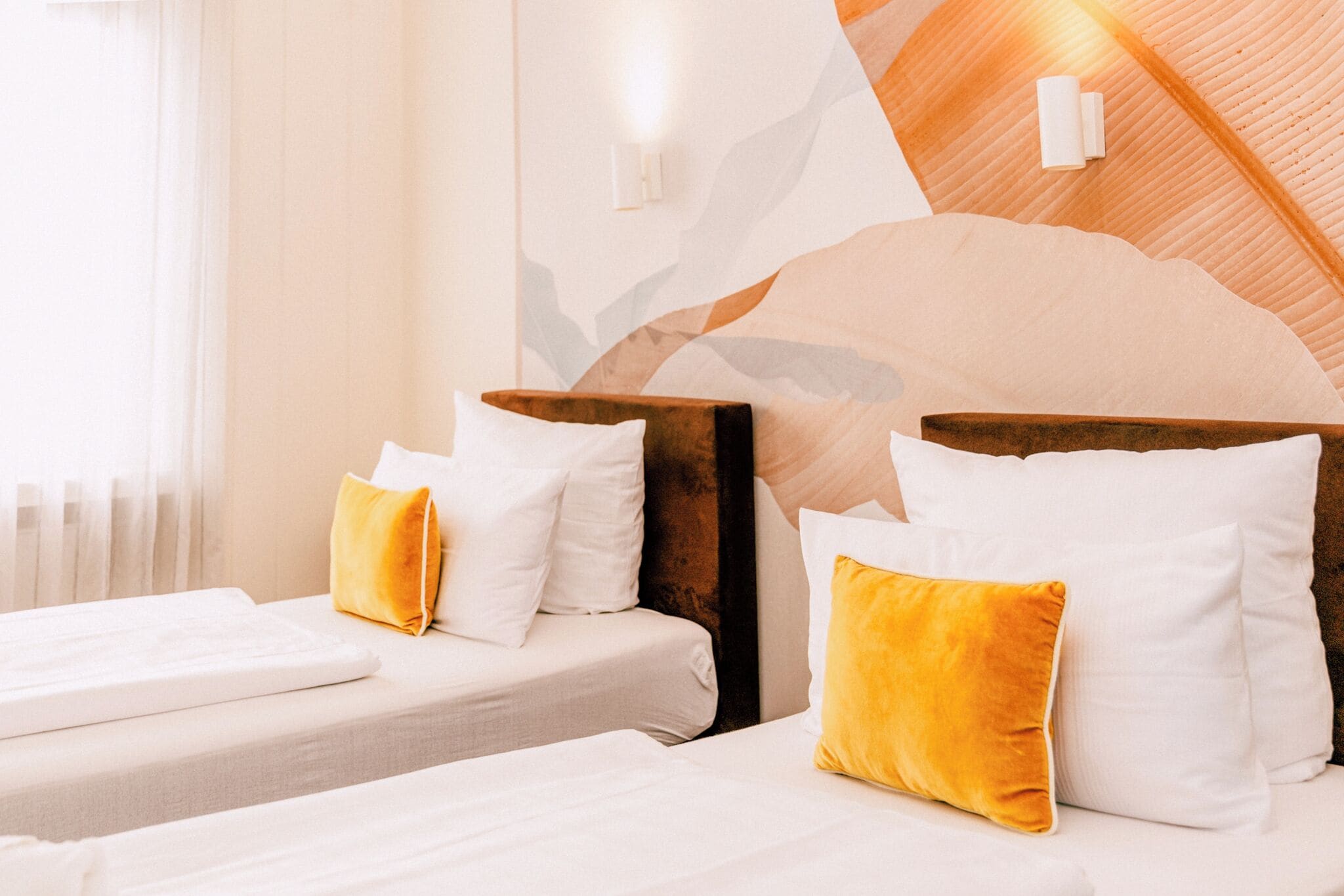 Habitación de hotel con dos camas, cada una con ropa de cama blanca y almohada amarilla. Hay una lámpara de pared sobre las camas y un diseño de pared texturizado detrás de ellas.