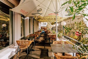An outdoor cafe with wicker chairs and tables under large umbrellas, with a view of a building in the background. - Hotel kleiner Markt Saarlouis (Saarlouis)
