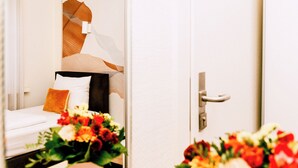 Habitación de hotel con cama, mesita de noche y espejo que refleja un ramo de flores.