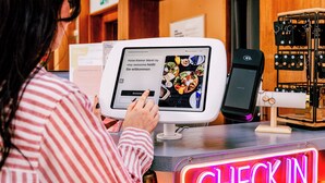 Una persona usando una tableta en la recepción de un hotel, con un cartel que dice 'CHECK-IN'.