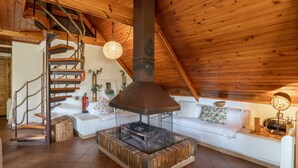 Un interior de madera con chimenea, sofá blanco y una escalera en espiral.