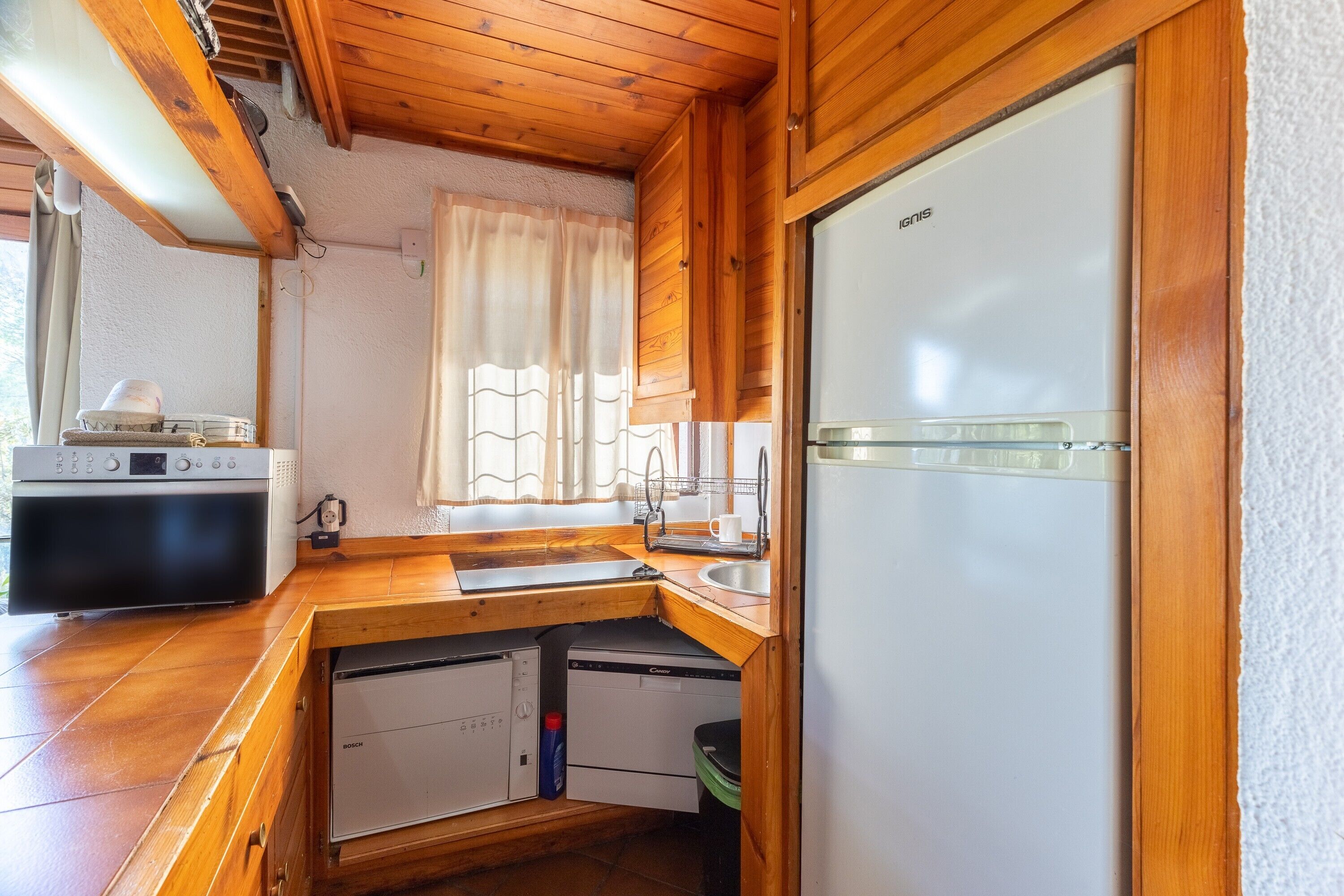 Een kleine keuken met houten kastjes, een ingebouwde oven, een vaatwasser en een koelkast.