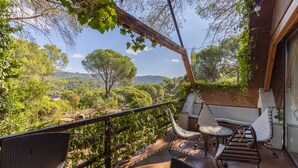 Un balcón con mobiliario de mimbre, una mesita y vistas a un paisaje exuberante.
