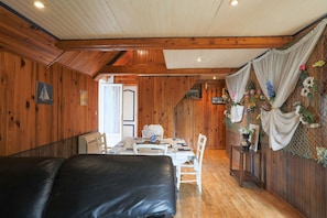Een houten interieur met een eethoek, een zwarte leren bank en een trap naar een andere kamer.