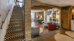 Un escalier avec des marches à carreaux, une porte en bois, une chaise rouge, une bibliothèque et un pouf à motifs.
