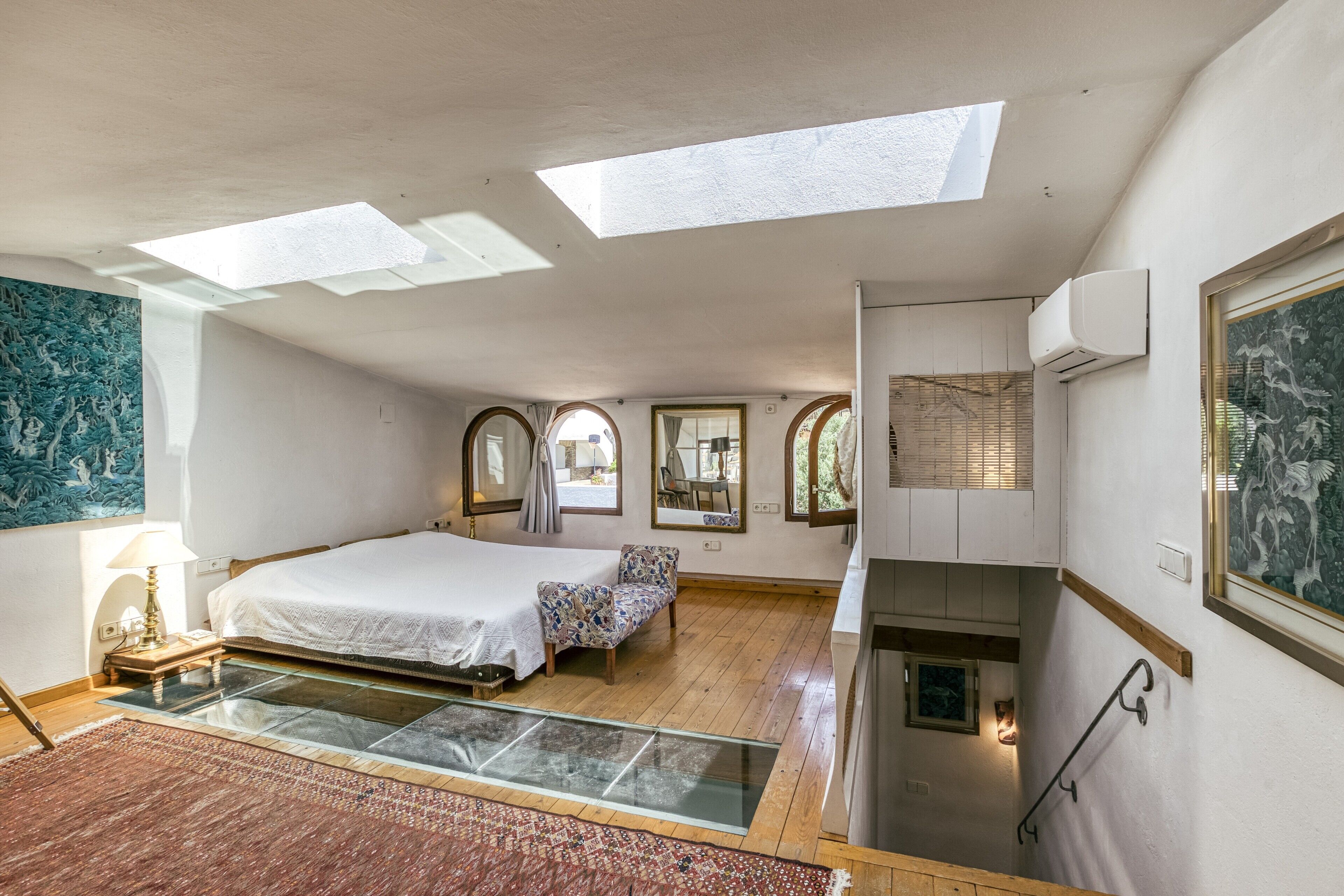 Une chambre avec des fenêtres de toit, un lit, une chaise, une petite table et un escalier.