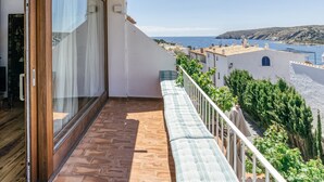 Un balcon avec vue sur la mer, un sol carrelé et un bâtiment blanc en arrière-plan.