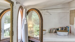 Une pièce avec un grand miroir, une fenêtre avec des rideaux, une lampe, une étagère remplie de livres et un panier.