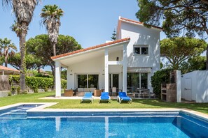 Una casa moderna con piscina, mobiliario exterior y palmeras.