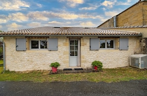 Une maison en pierre avec un toit en tuiles, une porte d’entrée et deux fenêtres avec des volets.