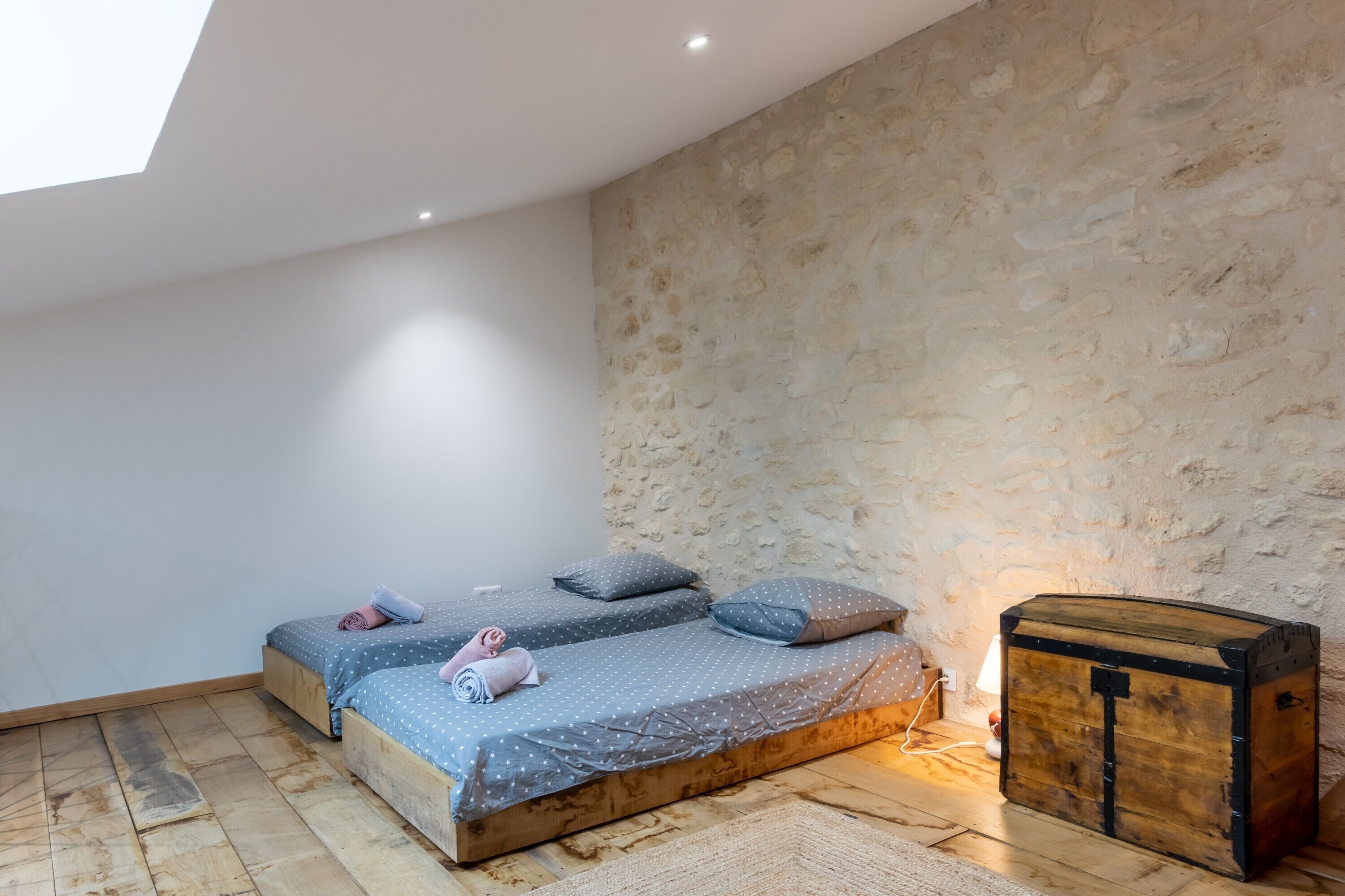 Ein Schlafzimmer mit zwei Betten, einer Steinwand, einer Holzkiste und einem Oberlicht.