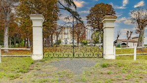 Une entrée fermée par un portail en fer forgé, un chemin de gravier et des arbres en arrière-plan.
