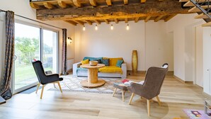Un salon spacieux avec un plafond en bois, un canapé, deux fauteuils, une table basse et une grande fenêtre.