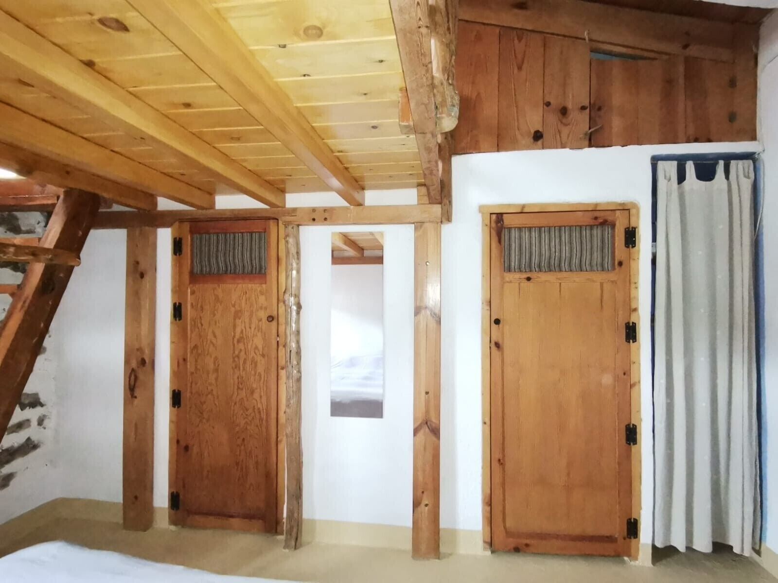 Una habitación con vigas de madera, dos puertas de madera, una ventana y una cortina.