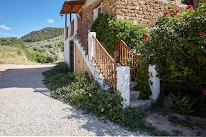 Un bâtiment en pierre avec une allée de gravier, un escalier en bois et une vue sur une colline.