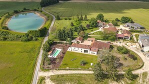 An aerial view of a rural property with a large pond, a swimming pool, and multiple buildings with red-tiled roofs.