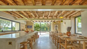 A modern kitchen with a bar area, wooden furniture, and large windows.