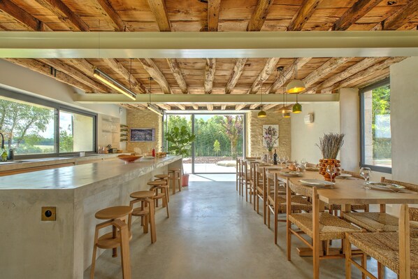 A modern kitchen with a bar area, wooden furniture, and large windows.