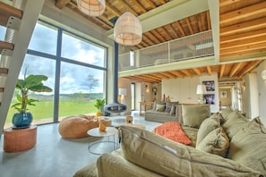 A spacious living area with a large window, a fireplace, and a high ceiling with exposed beams.