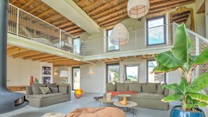 A spacious living area with high ceilings, a balcony, and a large potted plant.