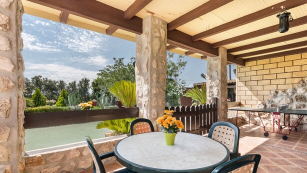 Un patio al aire libre con una mesa redonda, sillas, una planta en maceta y vistas a una piscina y jardín.