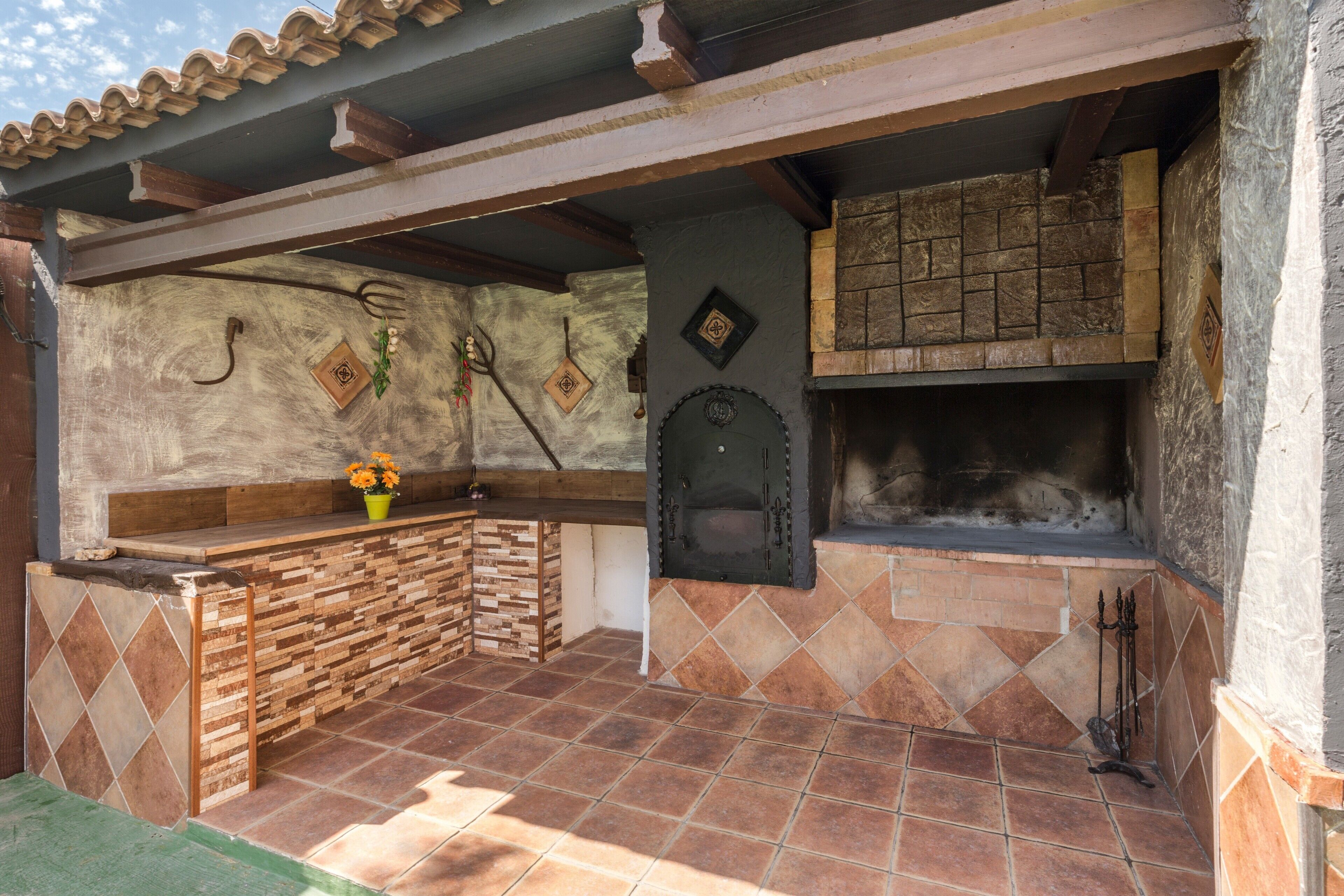 A rustic outdoor kitchen with a stone wall, a wooden counter, and a brick oven.