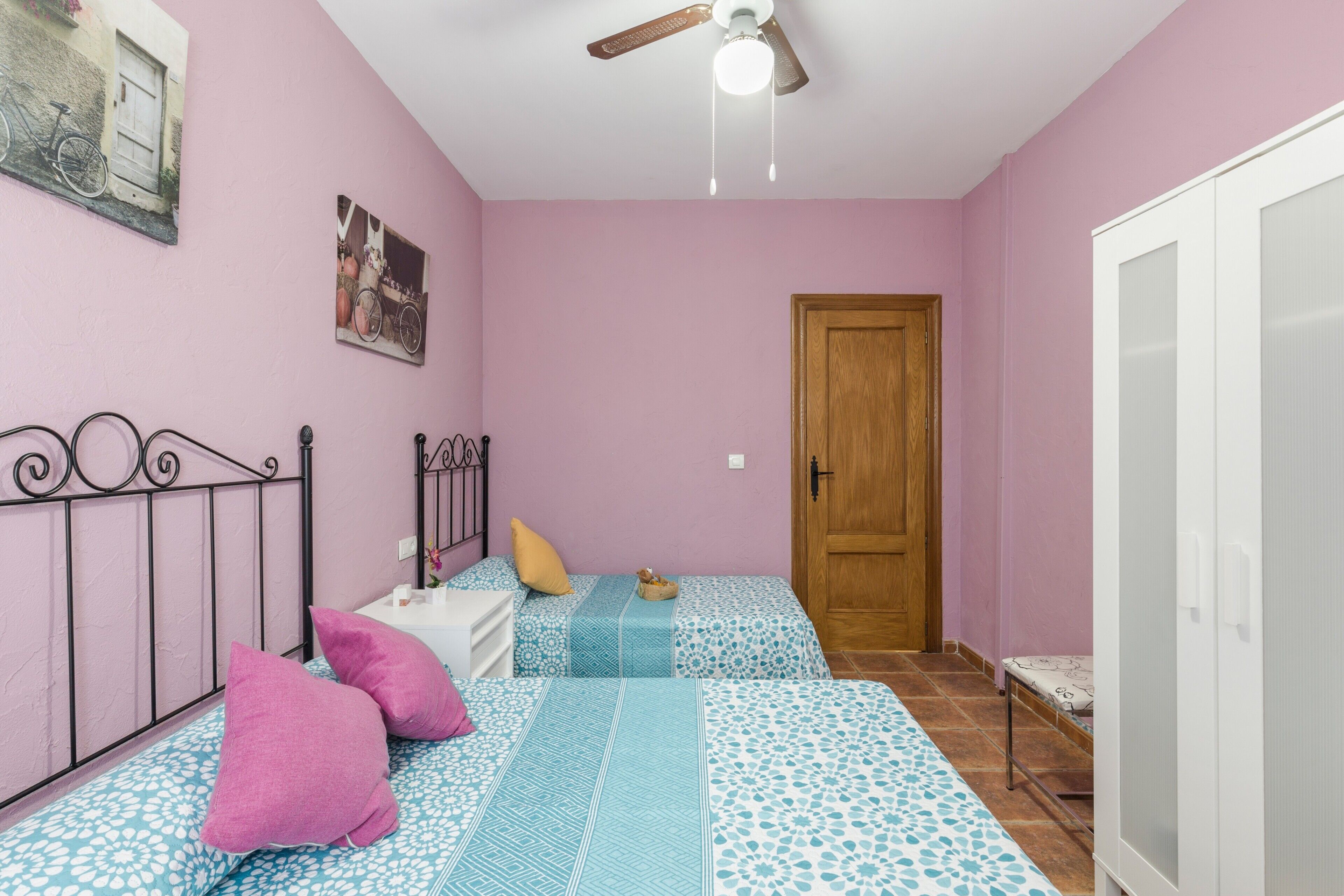 A bedroom with two beds, a ceiling fan, a wooden door, and a white wardrobe.