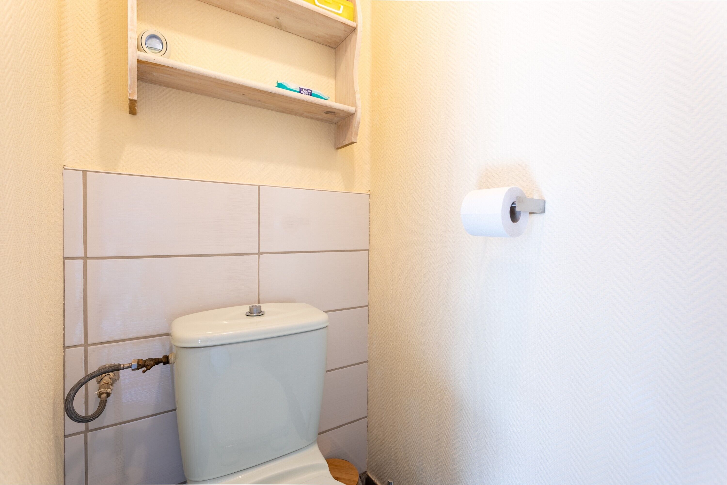 Een badkamer met een toilet, een plank erboven en een wc-papierhouder aan de muur.
