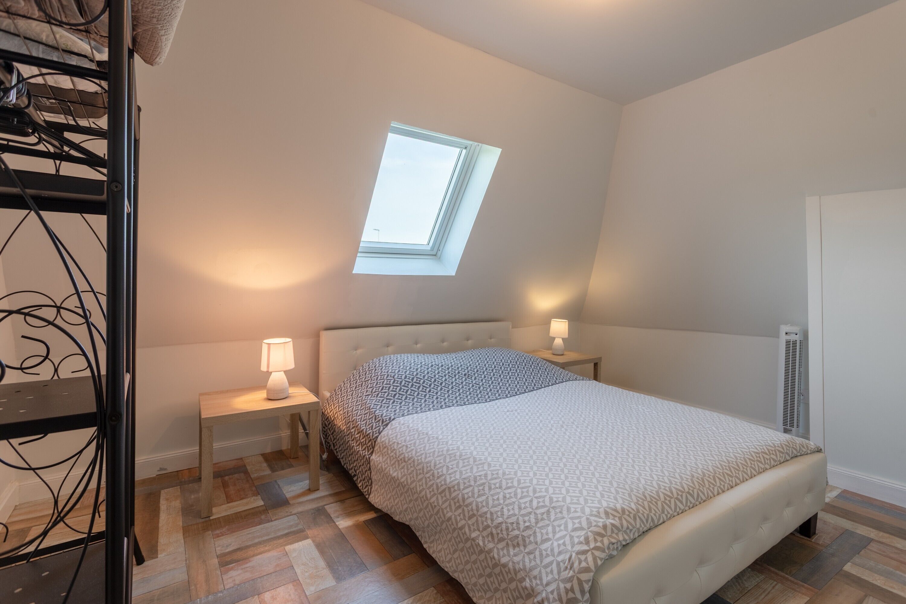 Une chambre à coucher avec un lit, une table de chevet, une lampe, un radiateur et une lucarne.