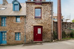 A stone building with a red door, a small window, and a blue window. - Holiday Home 'Les Mouettes Cancale' with Private Terrace and Wi-Fi (Cancale)