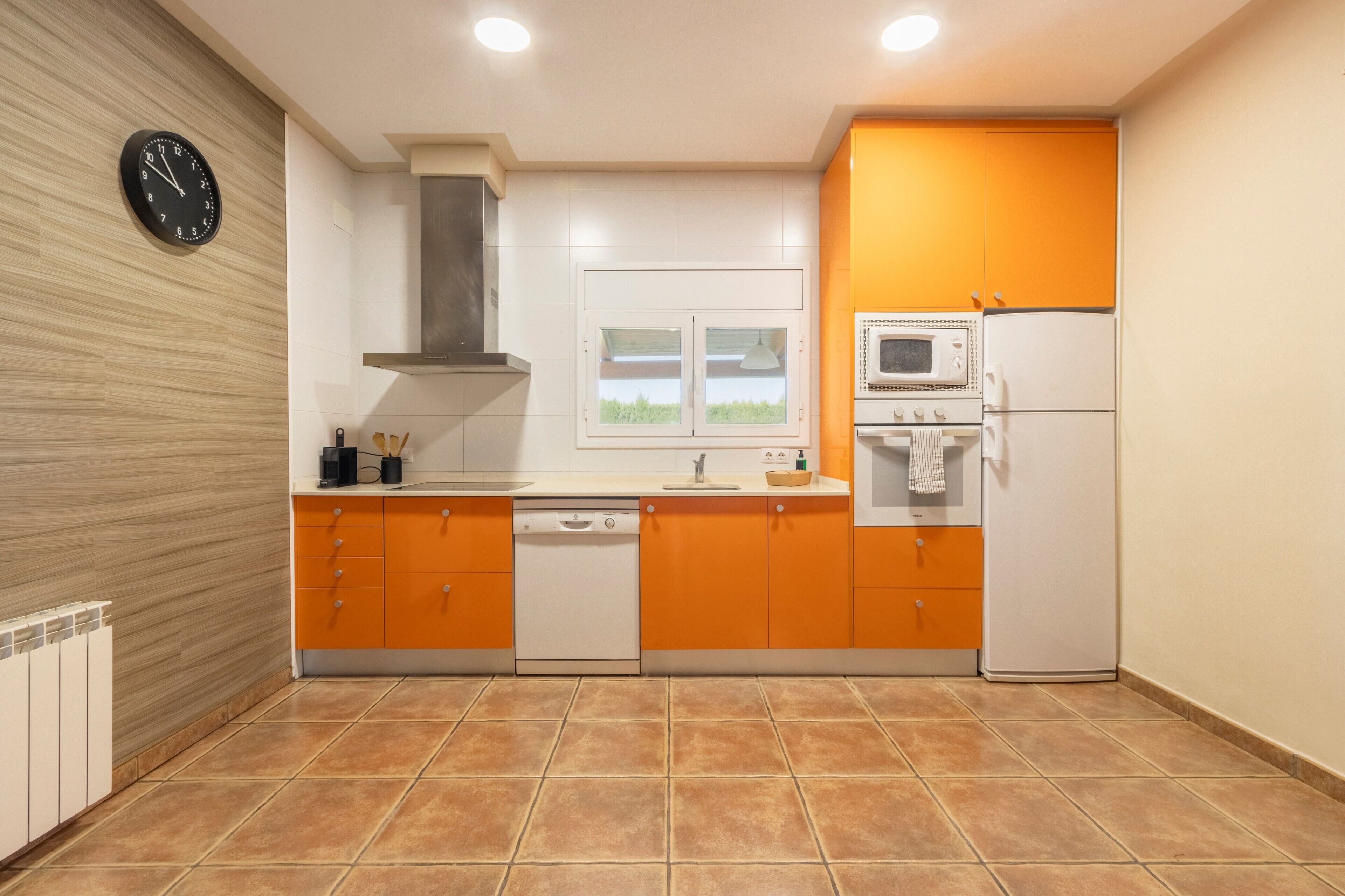 A modern kitchen with orange cabinets, a microwave, a dishwasher, and a clock on the wall.