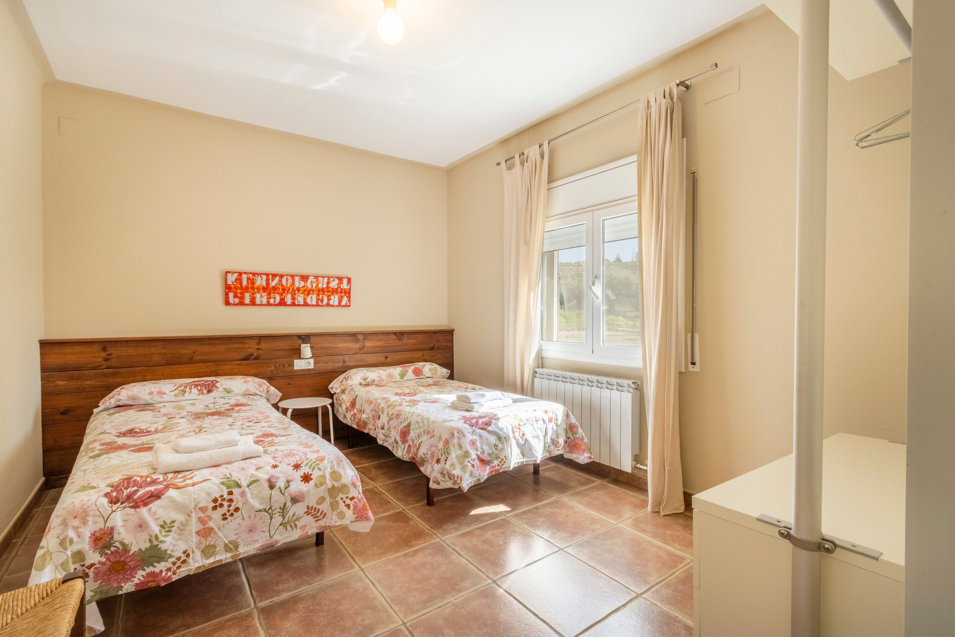 Een kamer met twee bedden, een raam met gordijnen, een radiator en een houten hoofdeinde.