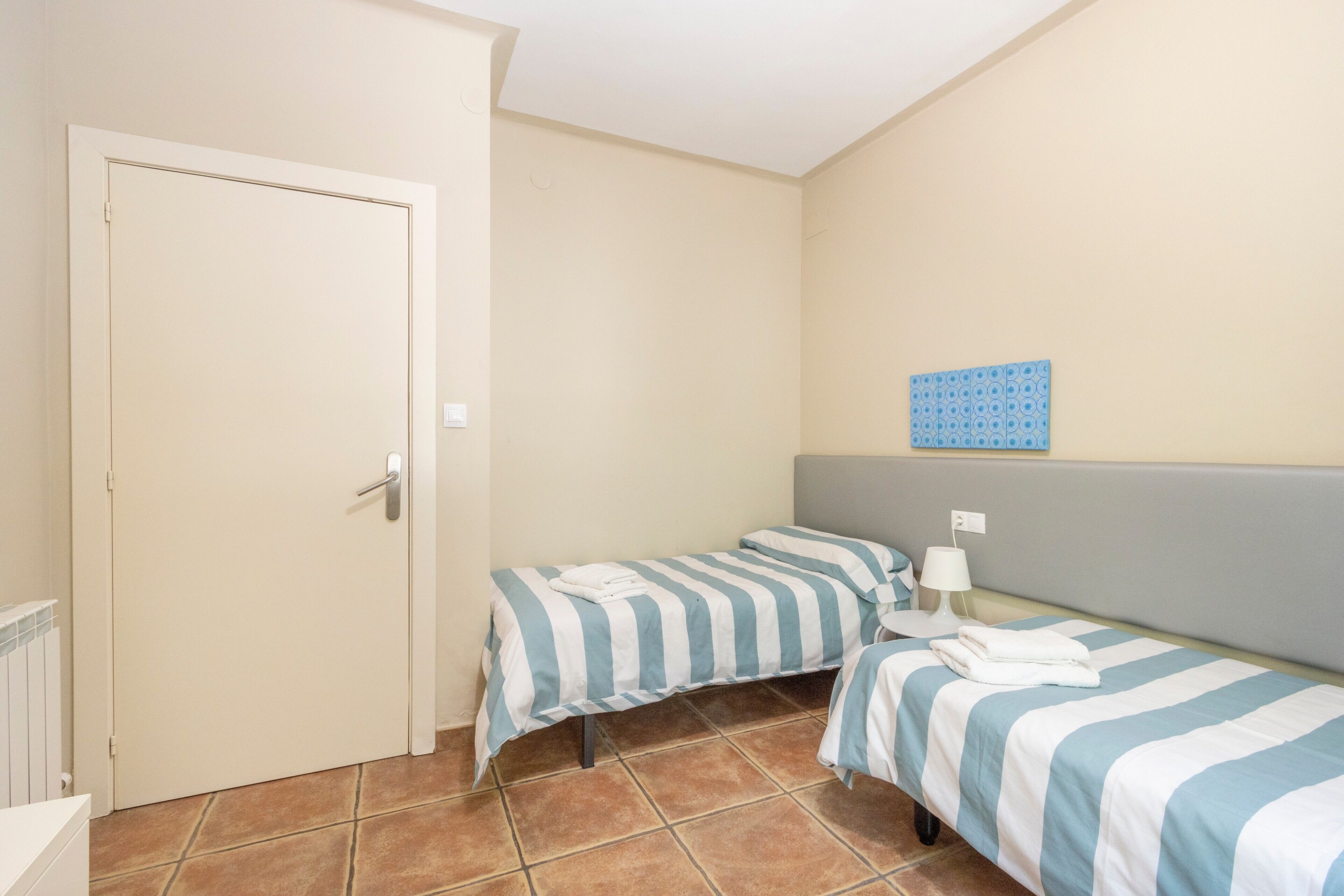 Une chambre avec deux lits simples, une porte, un radiateur et un luminaire fixé au mur.