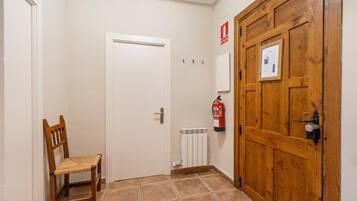 Een gang met een houten deur, een witte radiator, een brandblusser en een houten stoel.