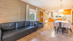 Ein modernes Wohnzimmer mit einer schwarzen Ledersofa, einem Esstisch mit Stühlen und einer Küche im Hintergrund.