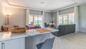 Eine moderne Küche mit Marmorarbeitsplatte, ein Essbereich mit Tisch und Stühlen, eine Sitzecke und große Fenster.
