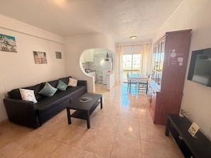 A living room with a sofa, a coffee table, a TV, and a dining area with a table and chairs. - Apartment 'Hilcity' with Shared Pool, Shared Garden and Balcony (Albufeira)