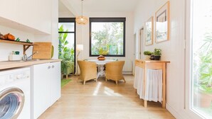 A compact kitchen with a washing machine, a dining area with wicker chairs, and a large window providing a view of greenery. - Holiday Home 'Art and Relaxation in Seville' with Private Terrace, Wi-Fi & Air Conditioning (Sevilla)