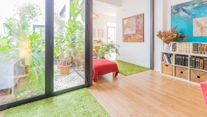 A modern living room with a glass door leading to a garden, a red sofa, a bookshelf, and a painting on the wall. - Holiday Home 'Art and Relaxation in Seville' with Private Terrace, Wi-Fi & Air Conditioning (Sevilla)