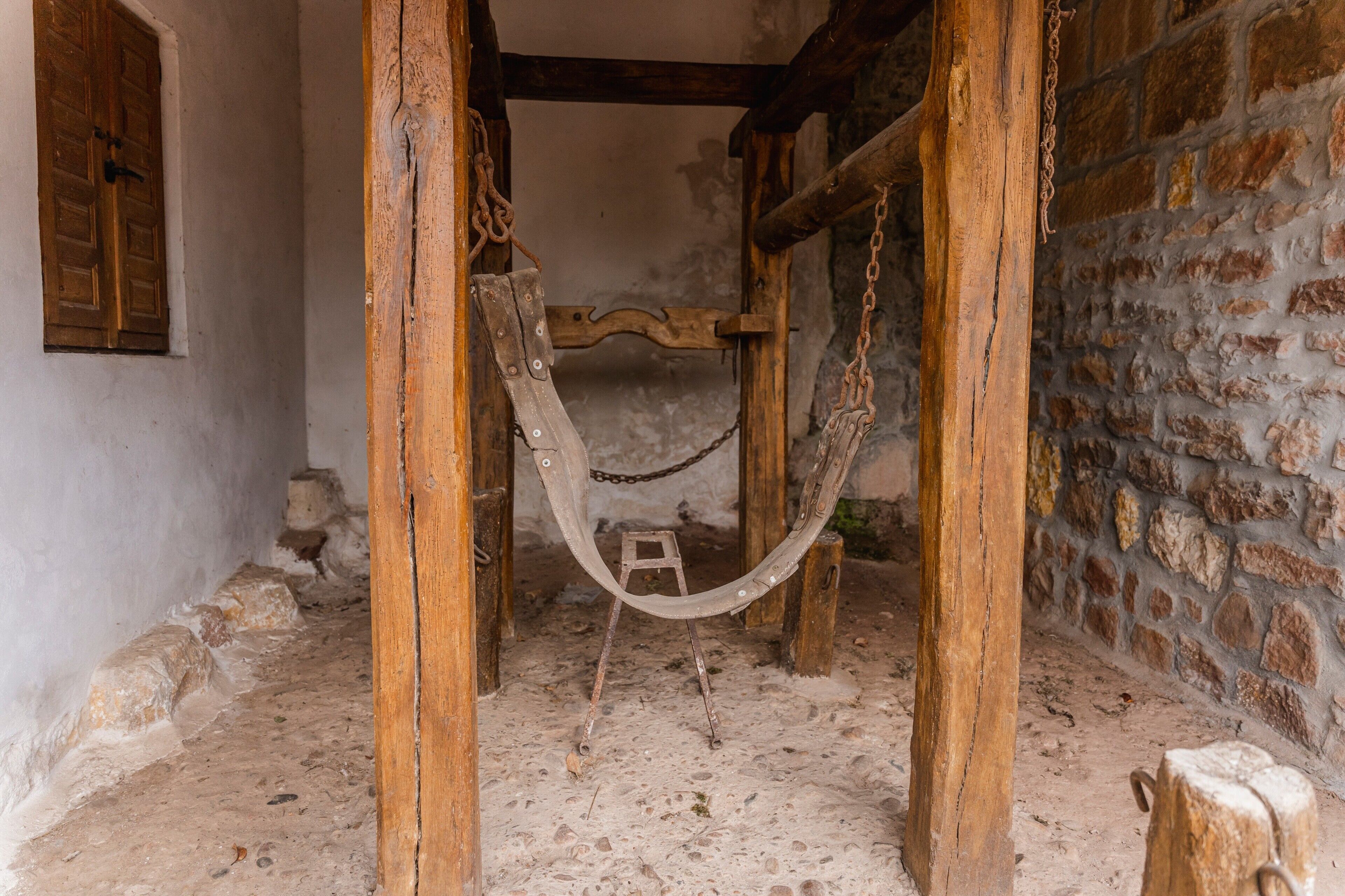 A rustic room with a wooden bed frame, a chain, and a small stool.