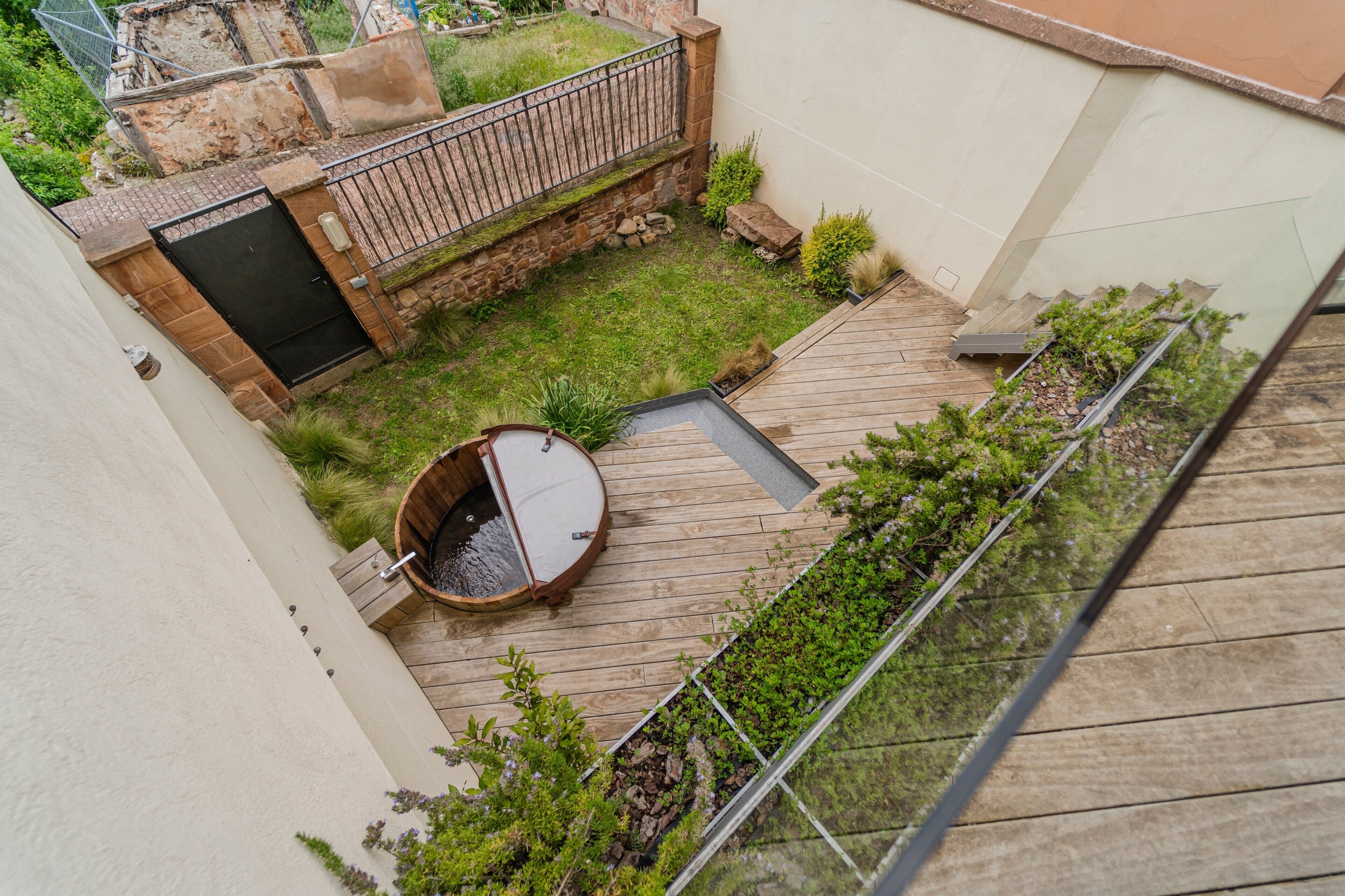 Un jardín en la azotea con jacuzzi, terraza de madera y un muro de piedra.