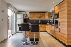 Une cuisine moderne avec des meubles en bois, des appareils électroménagers en acier inoxydable et deux tabourets de bar.