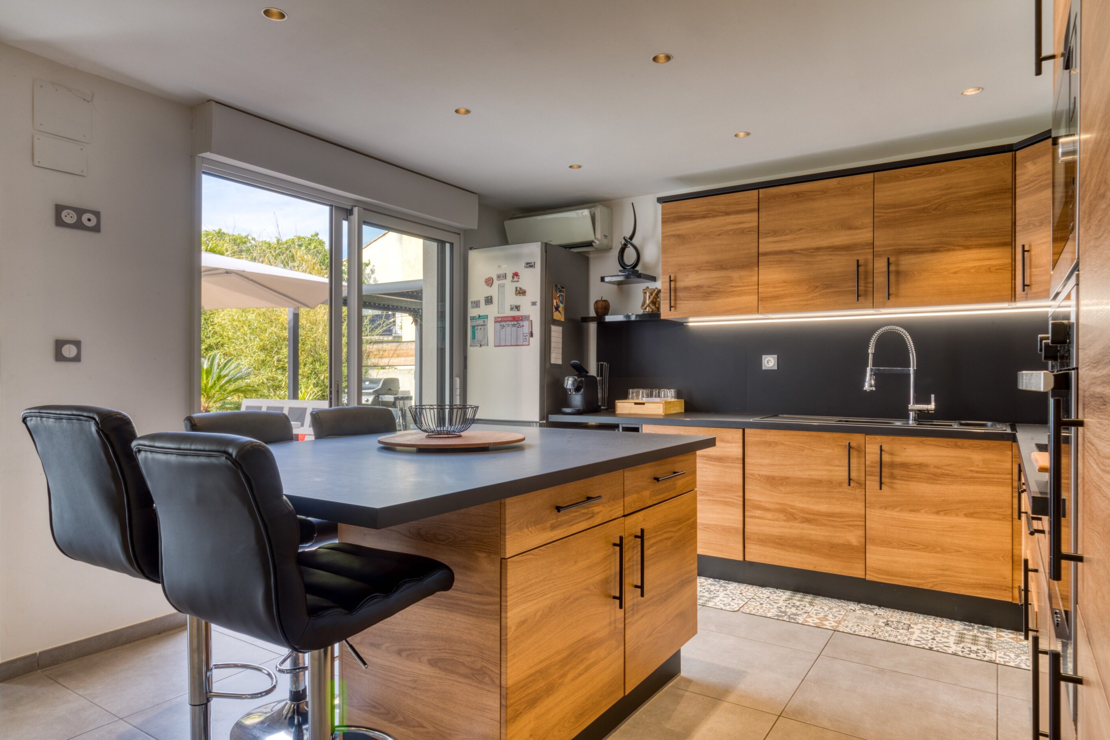 Een moderne keuken met houten kastjes, een zwart aanrecht en een groot raam.