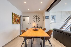 Un coin repas avec une table en bois, six chaises, une grande horloge murale et des œuvres d’art accrochées aux murs.