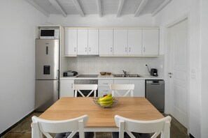 Una cocina con armarios blancos, un refrigerador de acero inoxidable, un microondas, un lavaplatos y una mesa de comedor con sillas.